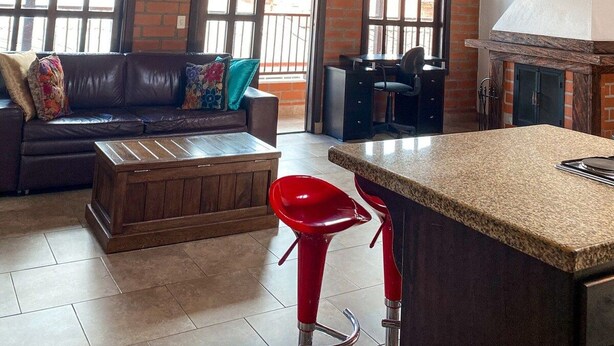 A spacious living area with a high wooden ceiling, a brick wall, and a kitchen with a marble countertop. - Apartamento Mas (Retiro)