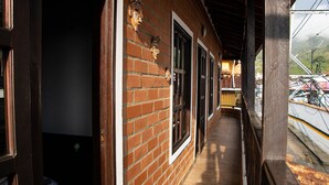 A brick building with a covered porch, large windows, and a view of parked cars and hills in the background. - Apartamento Mas (Retiro)