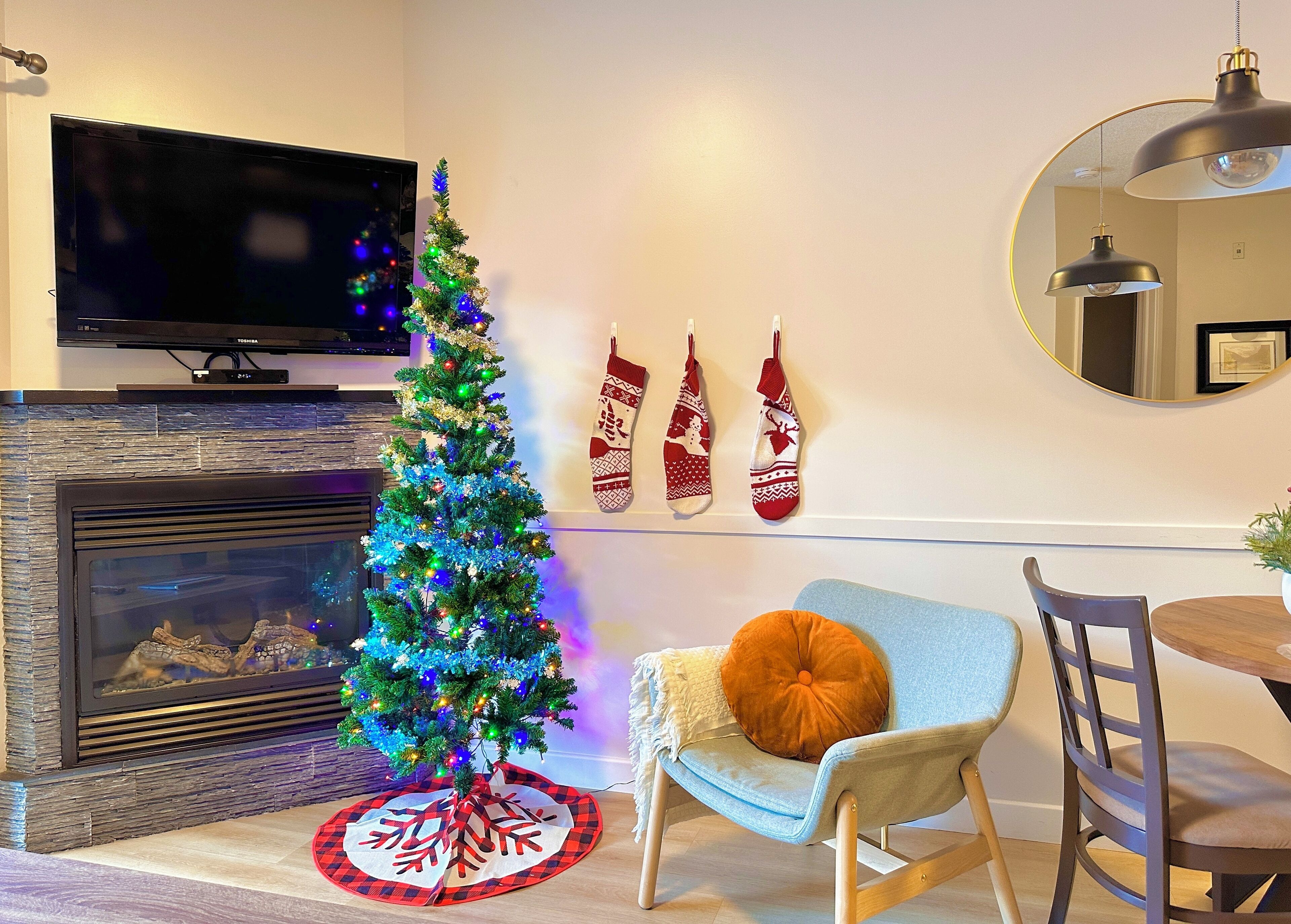 A living room with a fireplace, a Christmas tree, a television, and a dining area.