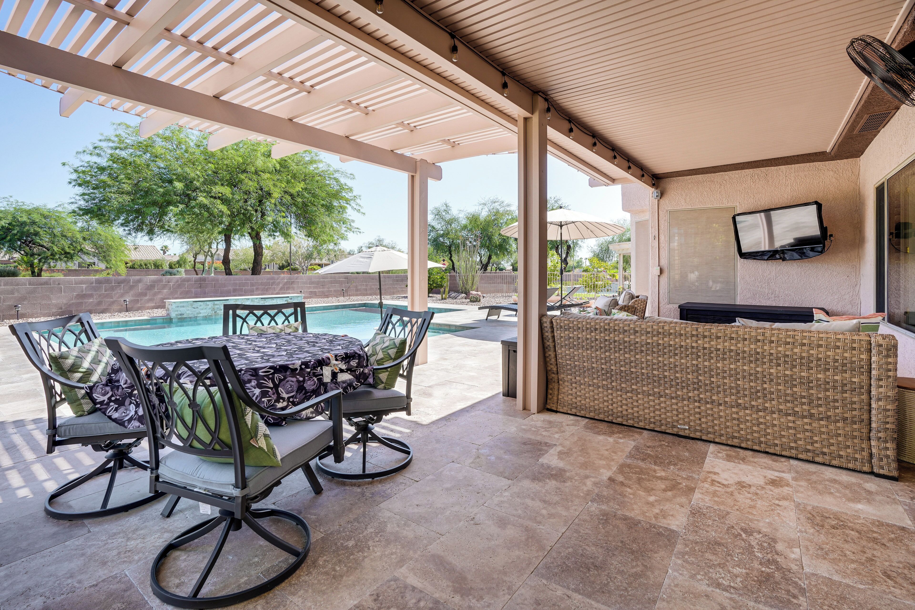 An outdoor patio with a pool, a dining table with chairs, and a bar area.