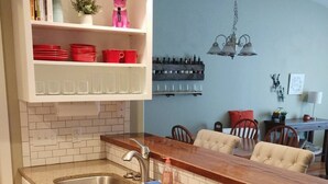 A kitchen with white cabinets, a granite countertop, a double sink, and a dining area with a table and chairs. - The Westside Nest - Cozy and Convenient! (Bozeman)