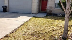 A residential house with a garage, a red door, and a small tree in the front yard. - The Westside Nest - Cozy and Convenient! (Bozeman)