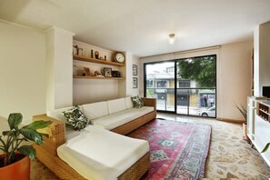 A living room with a sofa, a coffee table, a patterned rug, and a bookshelf with decorative items. - Memory Foam KING BED! Manila, El Poblado—Study, 300Mb Wifi, Dishwasher & Laundry (Medellín)