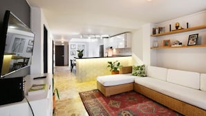 Una sala de estar moderna con un sofá, una televisión y una cocina al fondo.