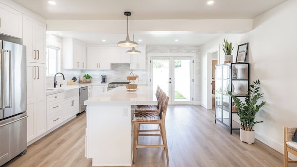 A modern kitchen with white cabinets, a central island, and a dining area with wooden chairs.