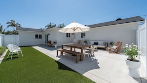 A patio area with a wooden table and chairs, a white umbrella, and a potted plant.