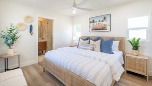 A bedroom with a bed, bedside tables, a ceiling fan, a window, and a door leading to a bathroom.