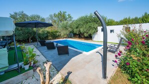 A swimming pool with lounge chairs and a sun umbrella, surrounded by greenery and a white building. - Gorgeous apartment in Pula (Pula)