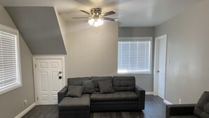 Ein geräumiges Wohnzimmer mit Ecksofa, einem zusätzlichen Sofa und Deckenventilator.