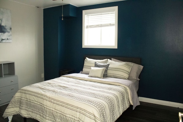 Un dormitorio con cama, mesita de noche, cómoda y ventana.