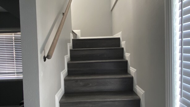 Eine Treppe mit dunklen Stufen und weißer Verkleidung, die zu einer Zwischenebene mit einem gerahmten Kunstwerk führt.