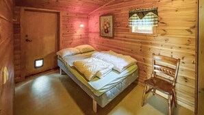 A wooden cabin room with a bed, a chair, a door, and a small window with a curtain. - 2 bedroom awesome home in Grue Finnskog (Grue Finnskog)