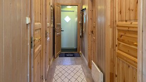 Ein Holzbodenkorridor mit einer Tür am Ende, einer Fußmatte und einer Leuchte darüber.
