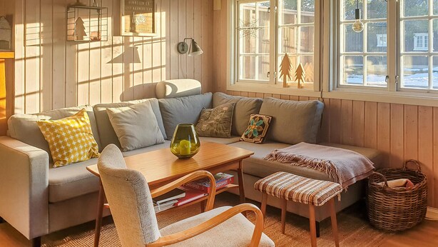 Ein gemütliches Wohnzimmer mit einer Couch, einem Couchtisch, einem Sessel und einem Fenster mit Blick auf Bäume.