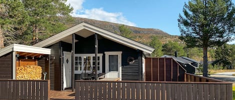 En stuga med en veranda, en möblerad uteplats och en hög med ved.