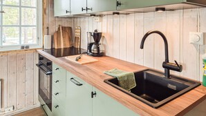 Eine Küche mit einem schwarzen Spülbecken, einer Holz Arbeitsplatte und grünen Schränken.