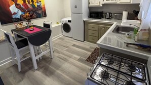 Cuina petita amb armaris blancs, fogó, microones i un rentapeus. Hi ha un quadre a la paret i una taula de dinar amb cadires.