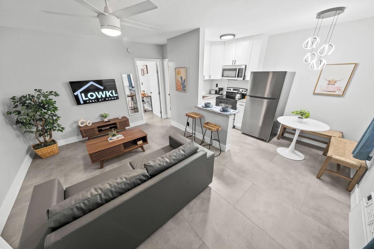 A modern apartment with a grey sofa, wooden coffee table, and a kitchen with white cabinets and stainless steel appliances.