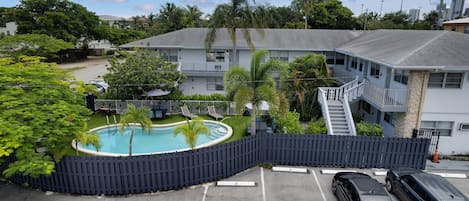 A pool area with a fence, a parking lot with two cars, and a building with balconies and a staircase.