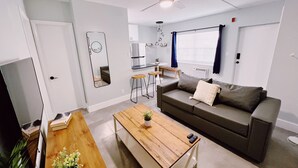 A modern living room with a sofa, coffee table, and a TV. There is a kitchen area with a fridge and a dining table. - Holiday Park by Lowkl (Fort Lauderdale)