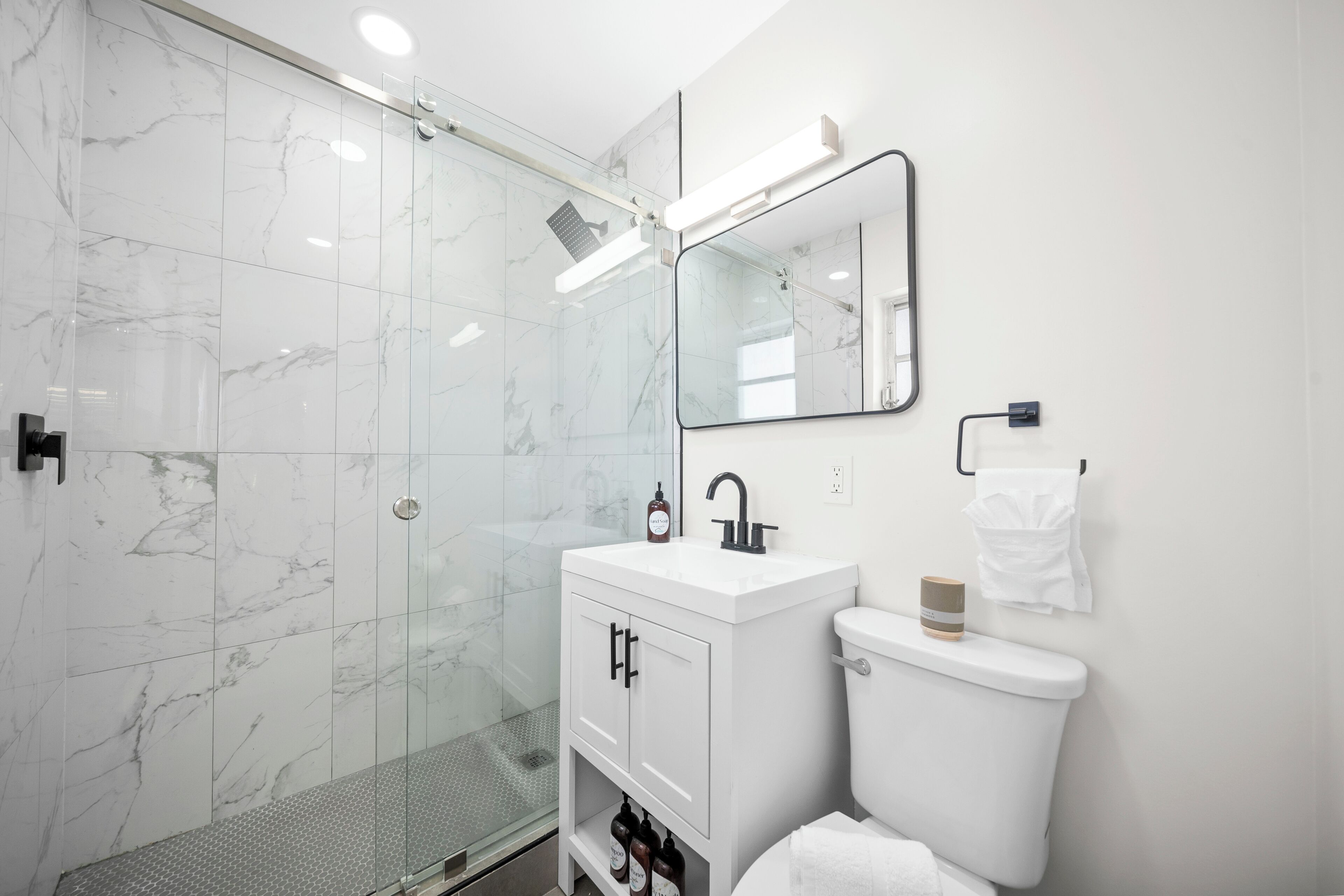 Uma casa de banho moderna com cabine de duche em vidro, toucador branco com espelho e sanita.