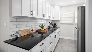 A modern kitchen with white cabinets, a black countertop, and a stainless steel refrigerator. - Holiday Park by Lowkl (Fort Lauderdale)