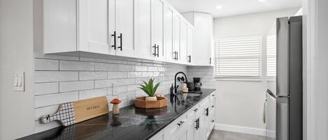 A modern kitchen with white cabinets, a black countertop, and a stainless steel refrigerator.
