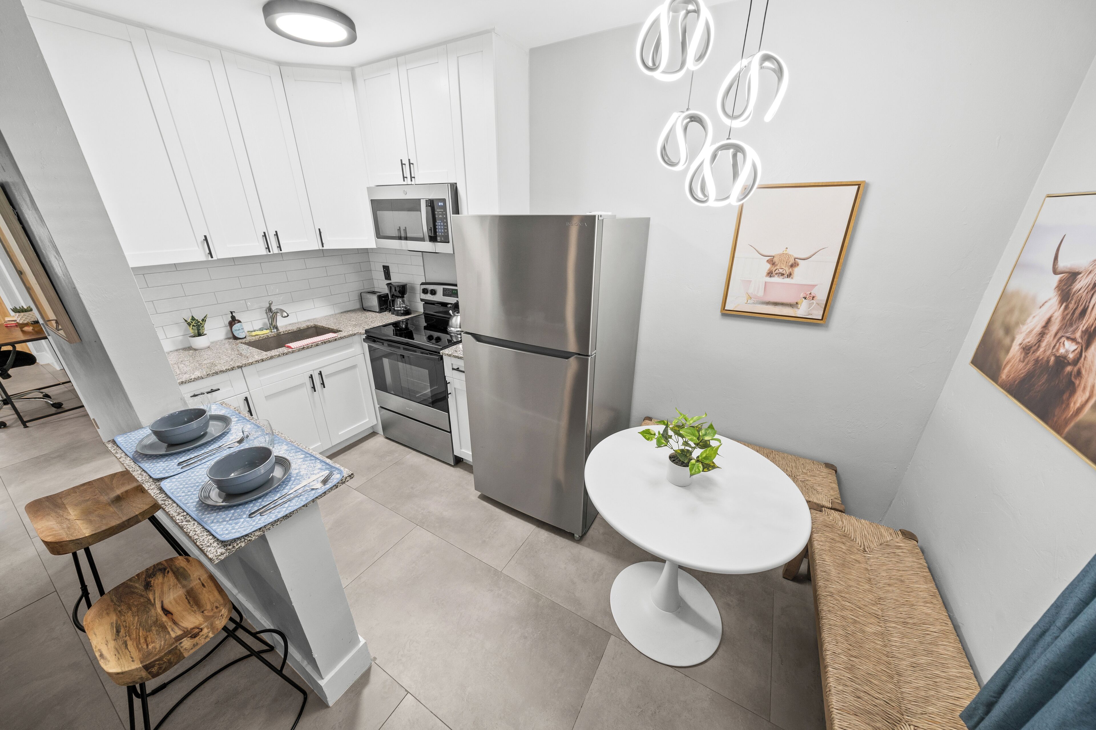 Una cucina moderna con mobili bianchi, elettrodomestici in acciaio inossidabile, una zona pranzo con tavolo rotondo e un’isola con sgabelli.