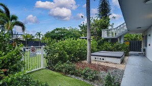 A modern outdoor area with a white gate, lush greenery, a palm tree, and a small building with a flat roof. - Holiday Park by Lowkl (Fort Lauderdale)