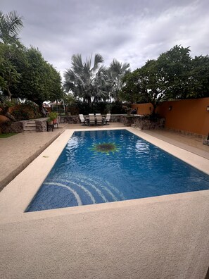 A rectangular swimming pool with a stone border, surrounded by a stone wall and a palm tree. - Located on El Cid golf course, private pool, minutes to the beach. (Mazatlán)