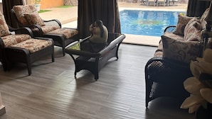 Ein Zimmer mit Blick auf einen Swimmingpool, Korbmöbeln und einem großen Fenster mit Vorhängen.