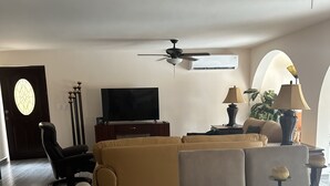 Ein modernes Wohnzimmer mit einer Couch, einem Glastisch, einem Deckenventilator und einem Fernseher.