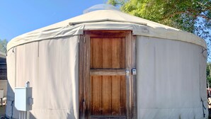 A yurt with a wooden door, a small porch, and a utility box.