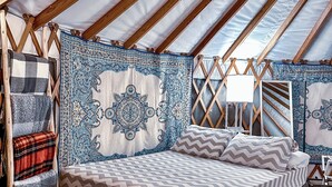 A cozy, well-lit tent with a bed, pillows, and a woven ottoman.