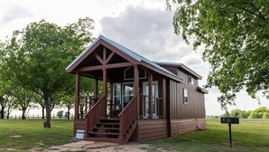 A rustic wooden cabin with a porch and stairs, surrounded by trees and open fields. - Exquisite Cabin, Enchanting Sunrises and Safari (Satin)