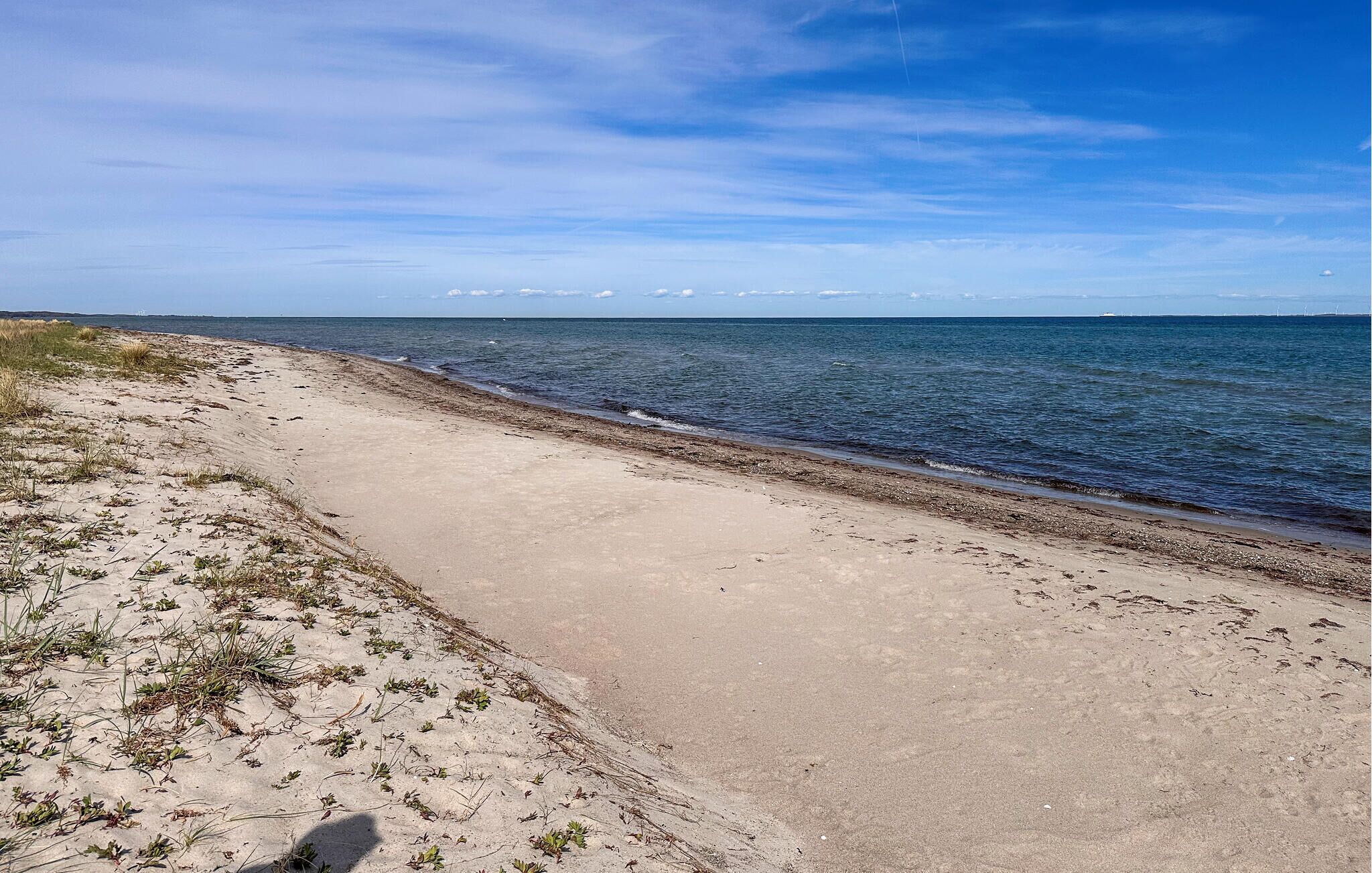 Una platja amb un camí de sorra que condueix a l'aigua, sota un cel clar i amb terra a la distància.