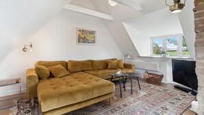 A cozy loft bedroom with a large window, a sofa, a small table, and a TV. - Lovely home in Rudkøbing with WiFi (Rudkøbing)