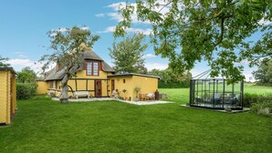A yellow house with a thatched roof, a glass greenhouse, and a well-maintained lawn. - Lovely home in Rudkøbing with WiFi (Rudkøbing)
