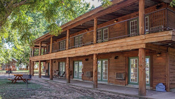 A rustic log cabin with a balcony, a picnic table, and a covered porch area. - Farm House Room #10 S (Satin)