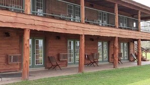 A wooden cabin with a porch, multiple windows, and outdoor seating. - Farm House Room #10 S (Satin)