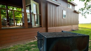 En grill framför ett trähus med en veranda och stora fönster.