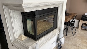 Un caminetto con cornice nera e vetri, incastonato in una cornice di marmo bianco.