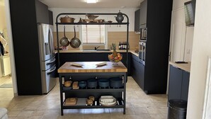 Una cucina moderna con isola centrale, mobili neri e un appendi-pentole a sospensione.