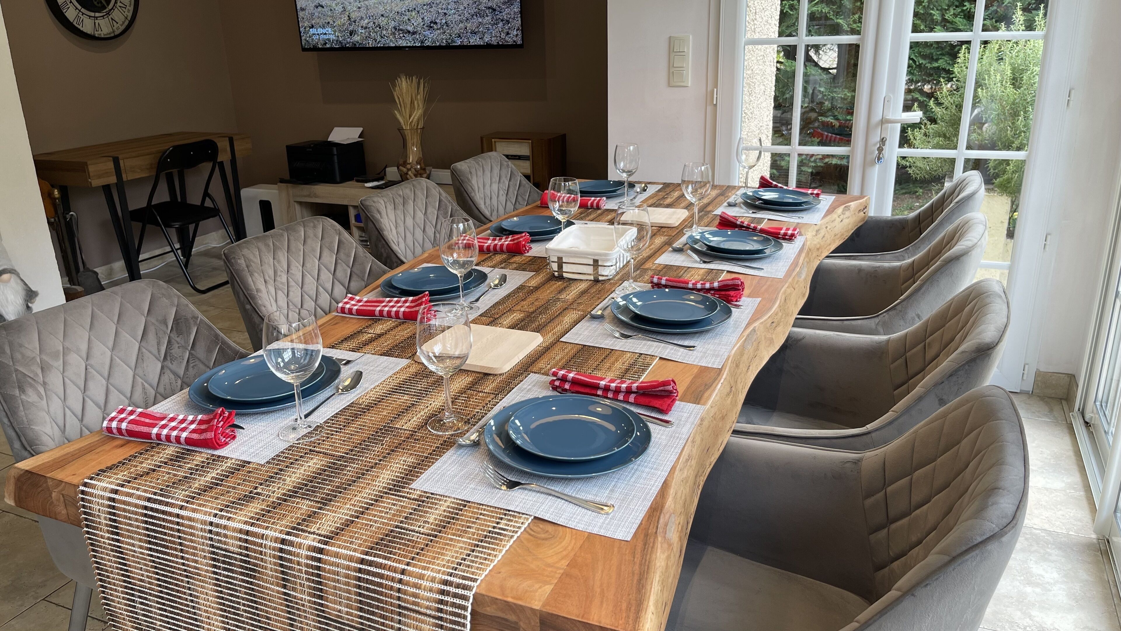 Un espace repas avec une longue table en bois, dressée pour six personnes, entourée de chaises rembourrées.