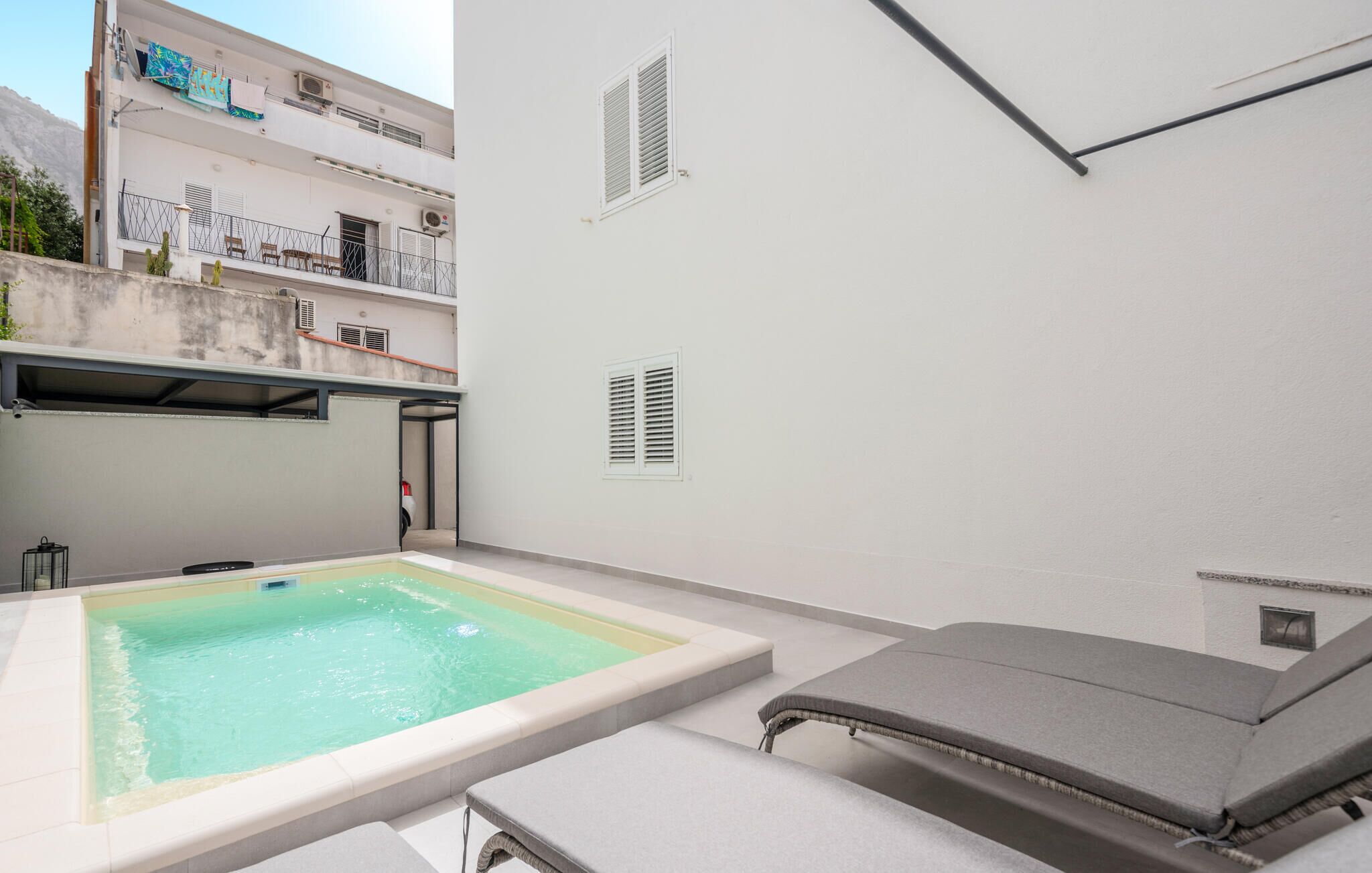 A clean, modern outdoor pool area with a hot tub, lounge chairs, and a view of a white building with balconies.