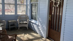 A porch with wicker furniture, a wooden door with a wreath, and a view of the street through large windows. - East Side Motel & Cabins (Mobridge)
