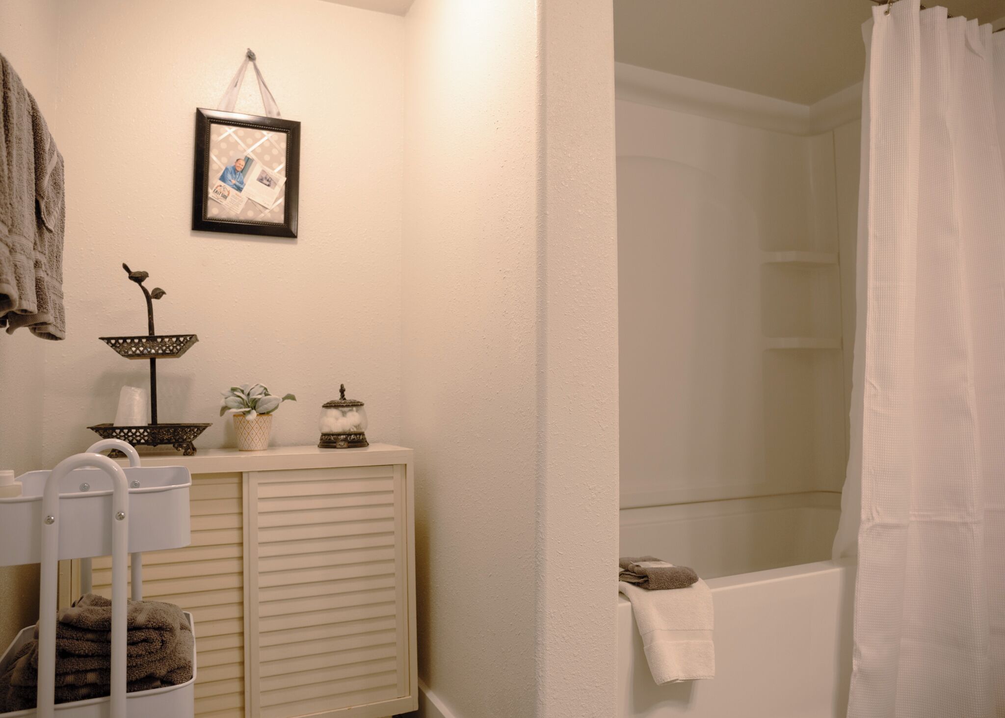 Un baño con bañera, lavamanos con espejo, toallero y una foto enmarcada en la pared.