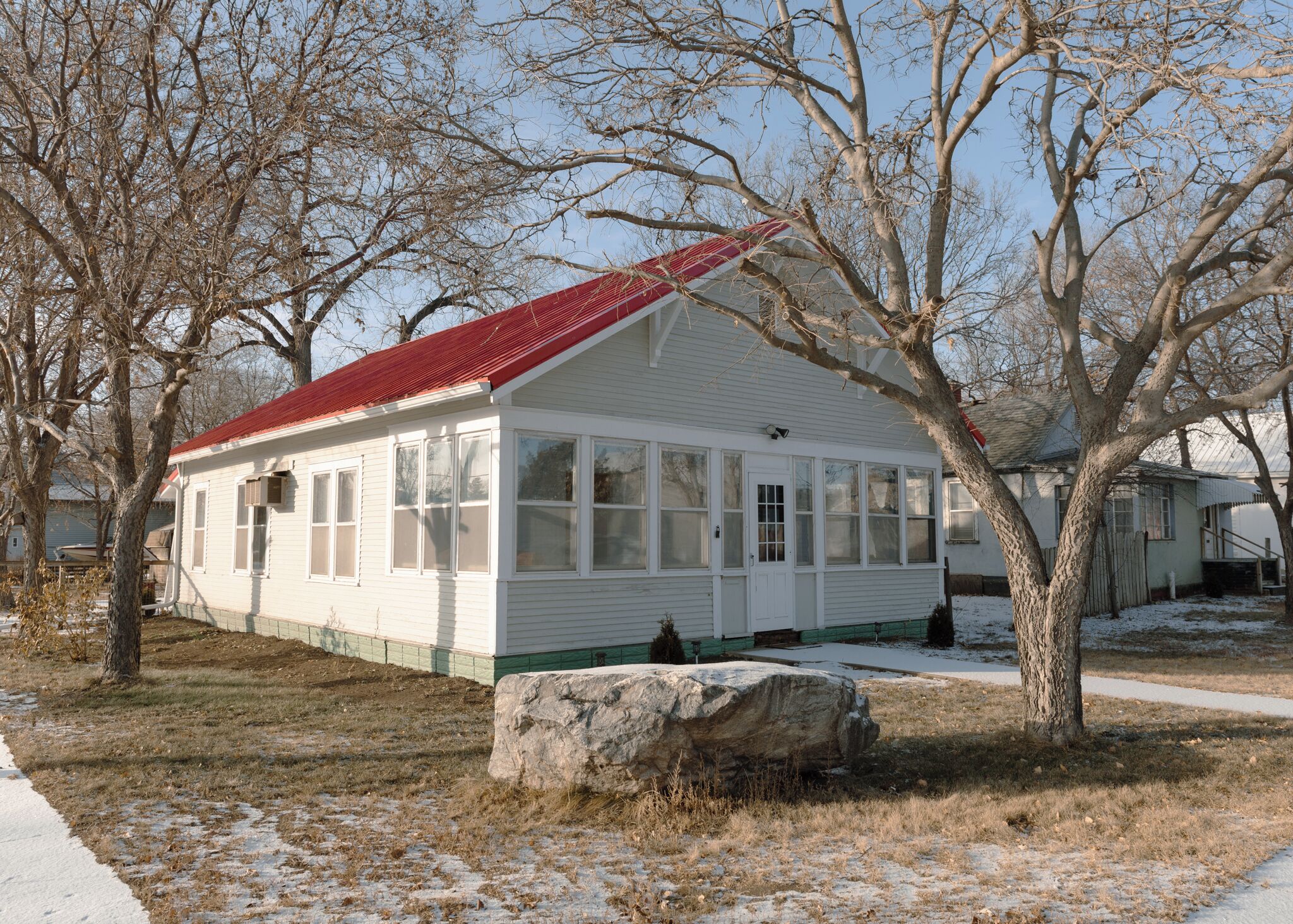 A white house with a red roof, large windows, and a porch.