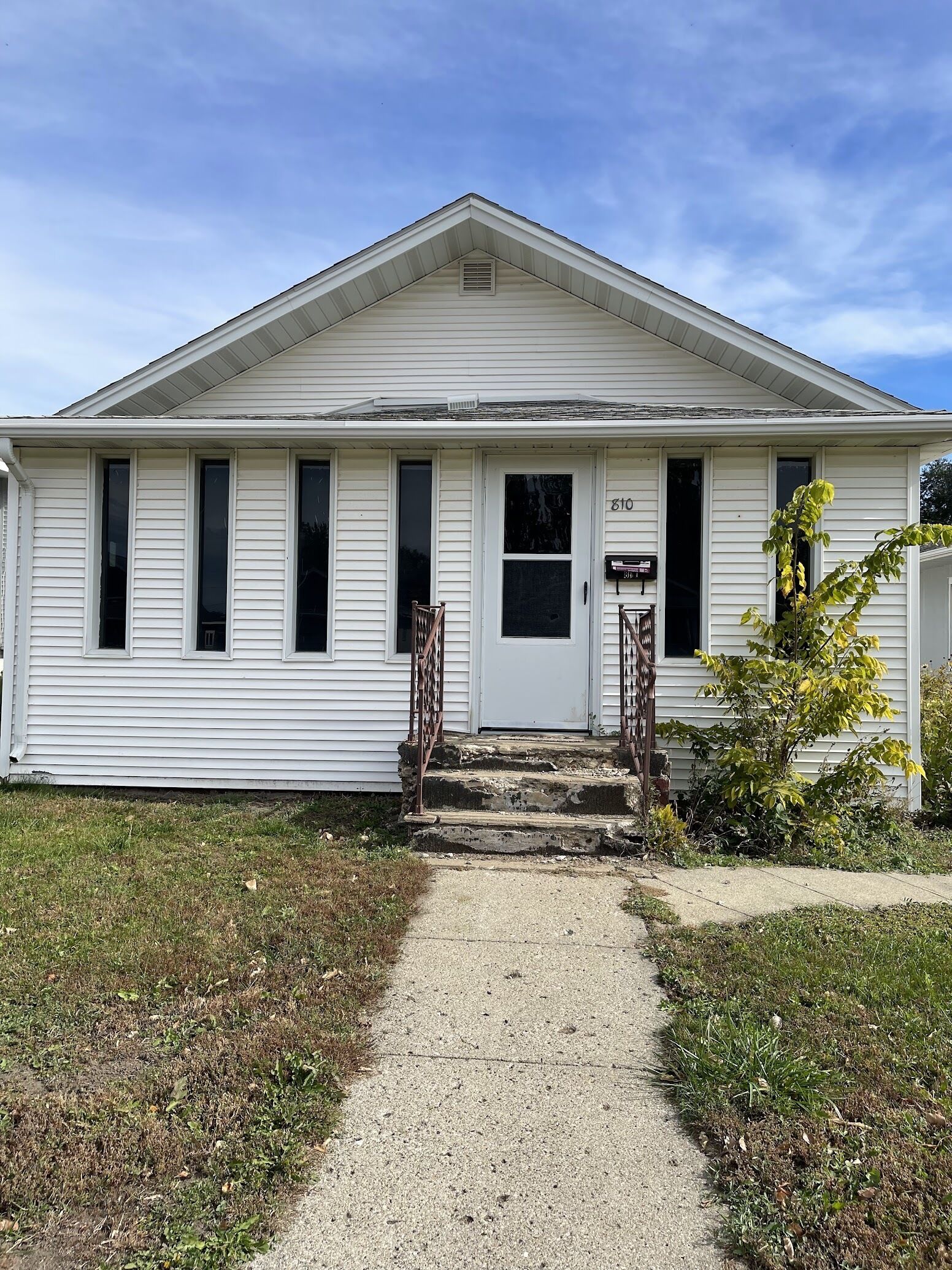 A single-story white house with a front porch, a small garden, and a gravel driveway.