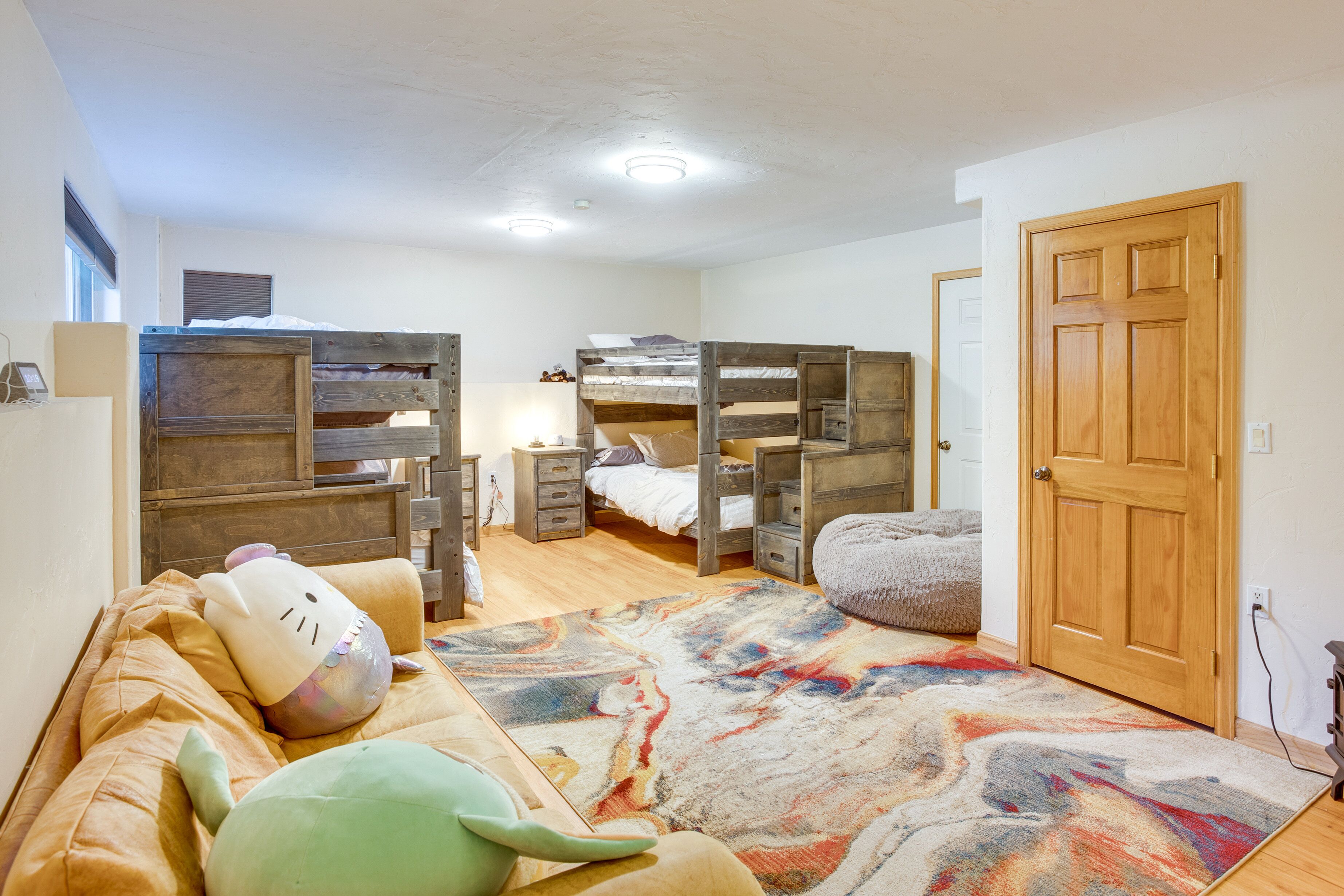 A dormitory room with bunk beds, a colorful rug, and a wooden door.